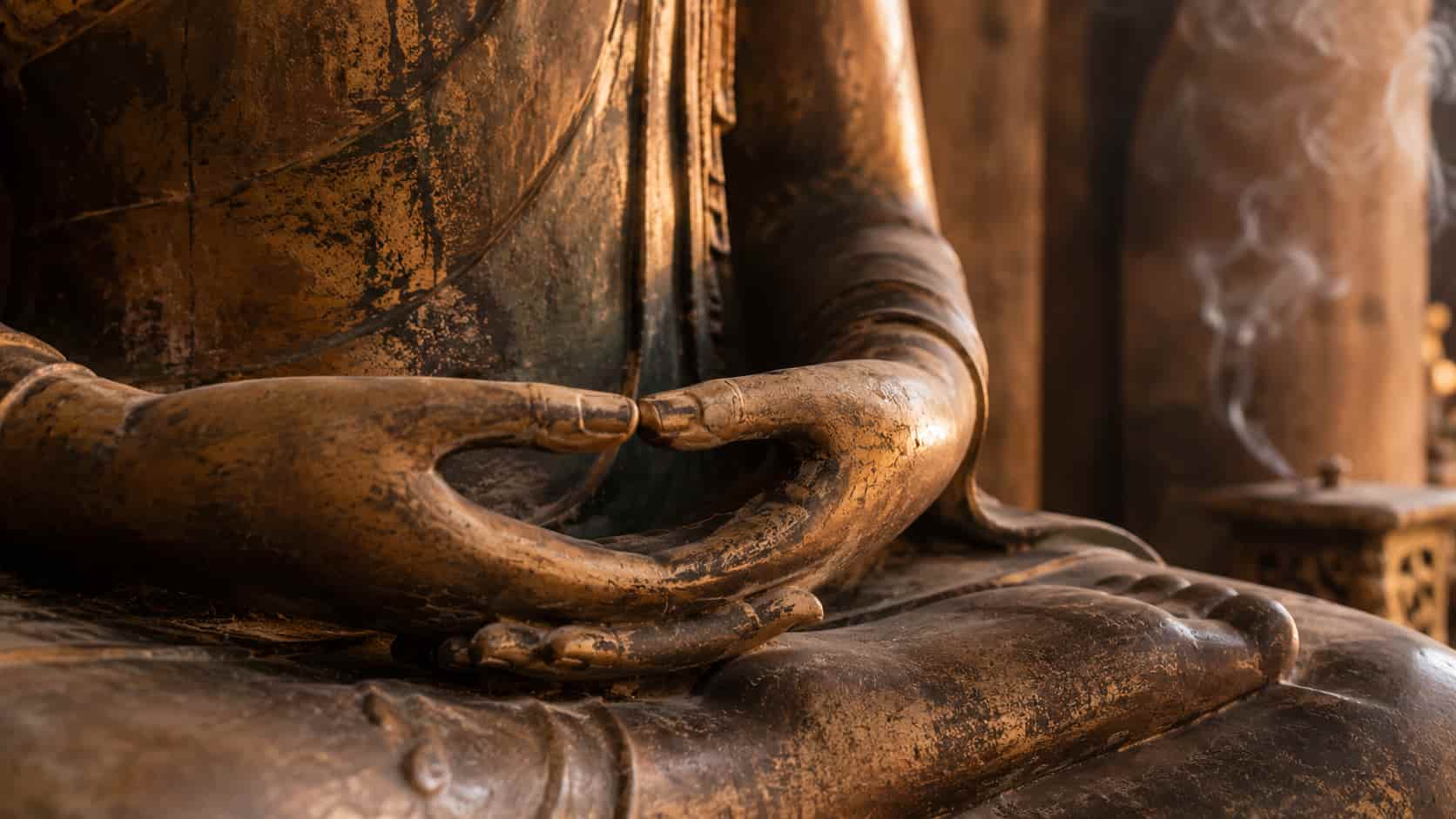 Close-up of a bronze Buddha statue's hands resting in the lap in a meditative Dhyana Mudra gesture.