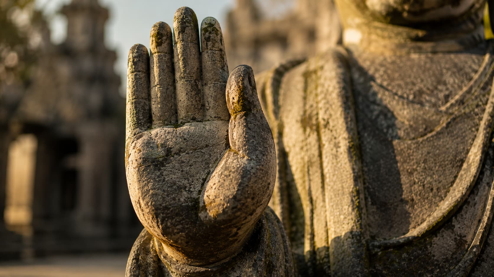 Close-up of a weathered stone Buddha statue's raised right hand showing the Abhaya Mudra gesture of fearlessness.