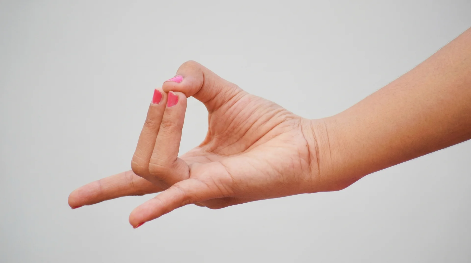 Close-up of a person's hand in Apana Mudra, with the tips of the middle and ring fingers touching the thumb while others extend.