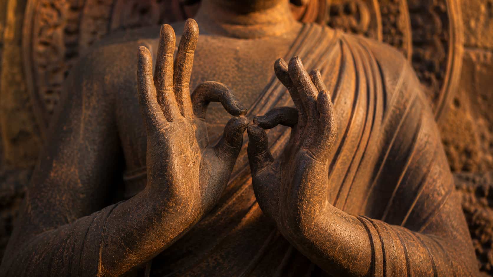 Close-up of a stone Buddha statue’s hands held at chest level forming the Dharmachakra Mudra wheel-turning gesture.