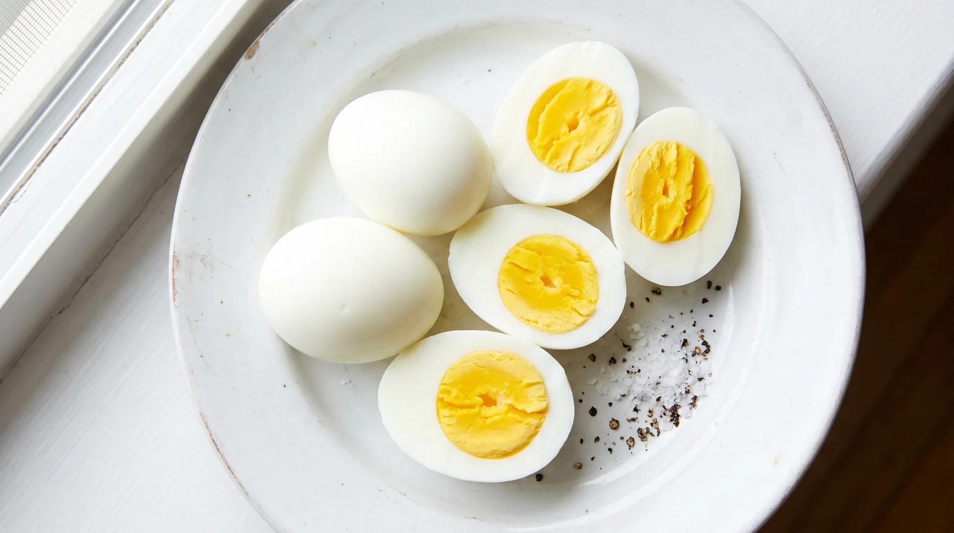 Sliced hard-boiled eggs with visible yellow yolks arranged on a white plate sprinkled with a pinch of sea salt.