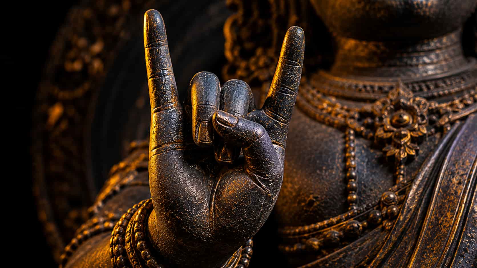 Close-up of a dark bronze statue's hand raised with index and pinky fingers extended in the Karana Mudra gesture.