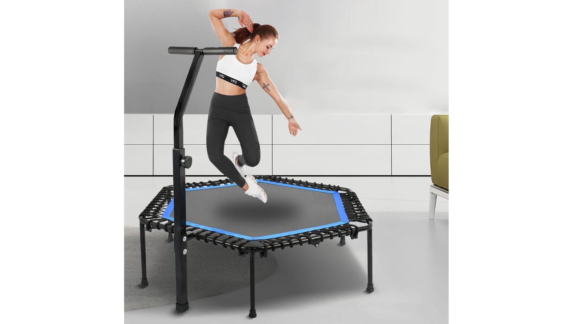 A woman in a sports bra and leggings jumping mid-air on a black and blue OZFIT mini trampoline with a handlebar.
