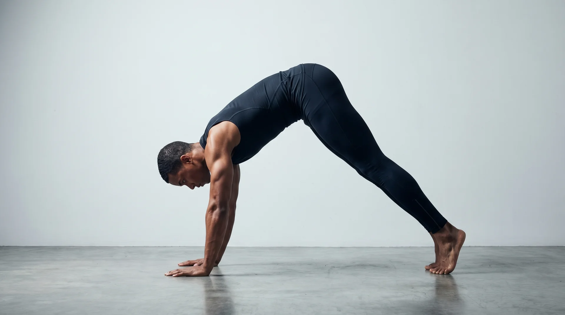 A side-view of a man with short dark hair performing a pike push-up position on a light-colored floor in a bright studio.