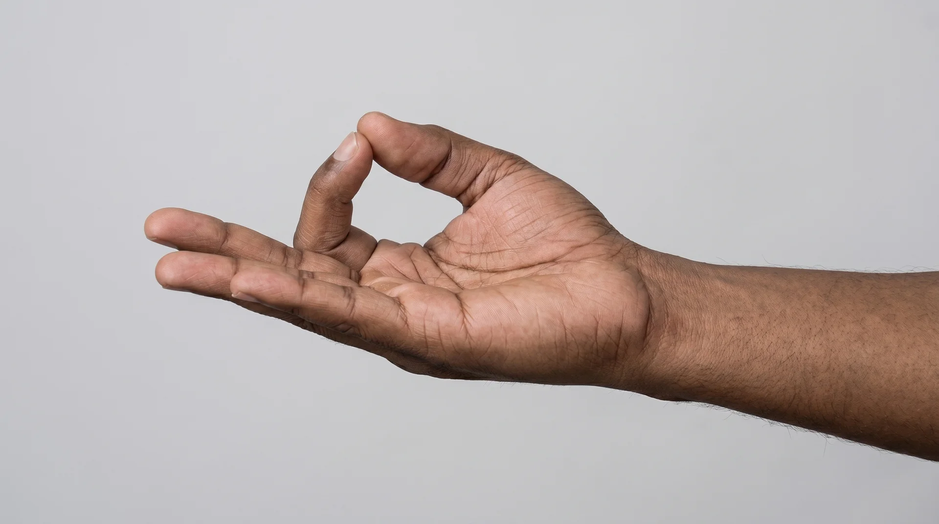 Close-up of a person's hand in Shuni Mudra, with the tip of the middle finger touching the thumb while the other fingers are extended.