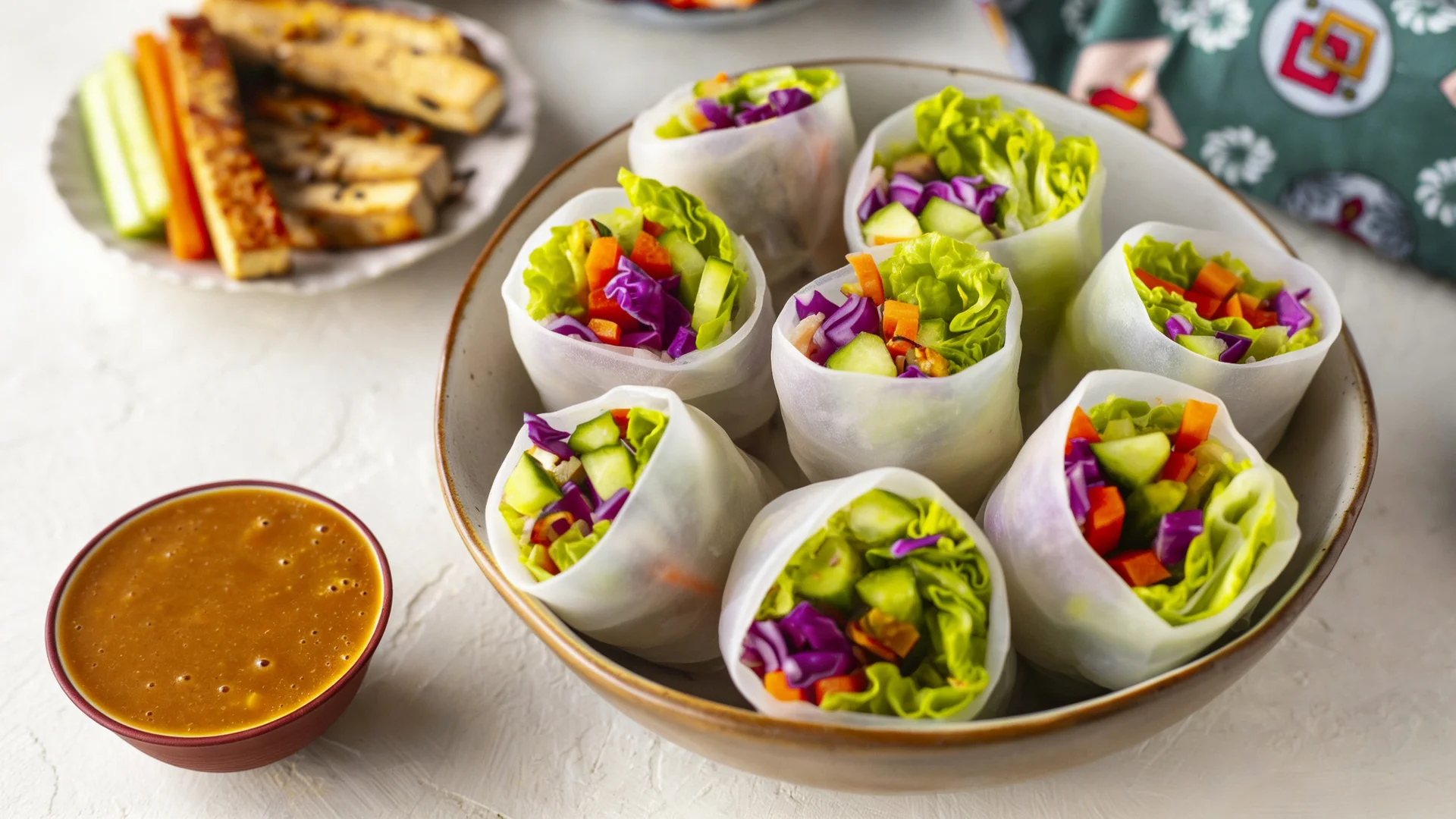 A plate filled with several fresh rice paper rolls packed with purple cabbage and greens, served with peanut sauce.