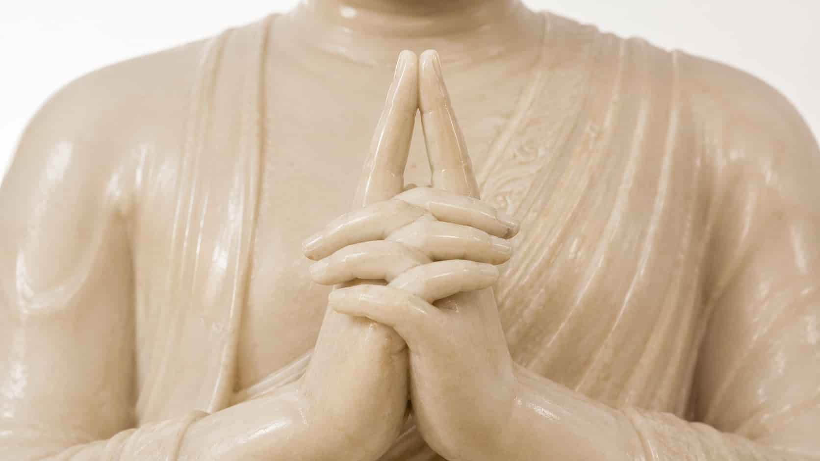 Close-up of a white stone Buddha statue's hands at chest level, with index fingers pressed together pointing upward.