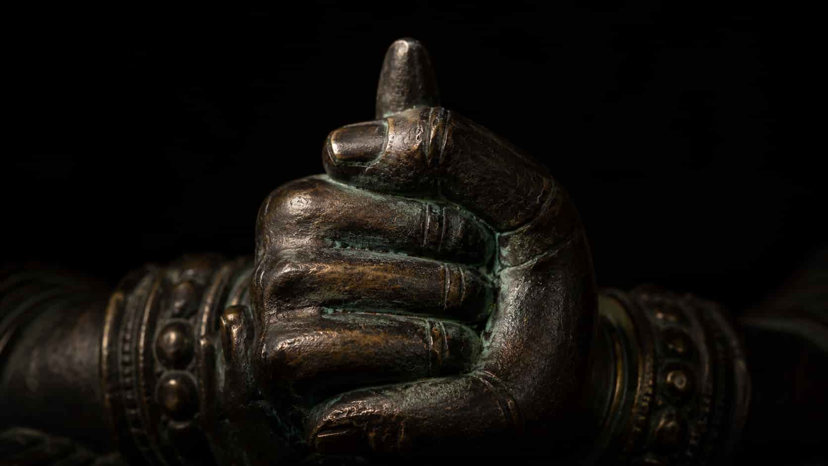 Close-up of a bronze statue's hands forming the Vajra Mudra, with the right index finger enclosed within the left fist.
