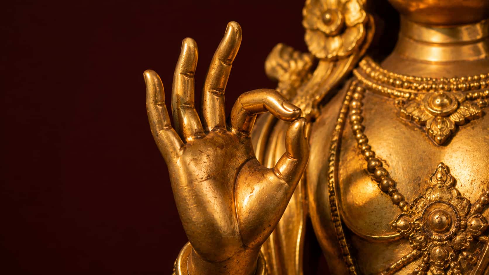Close-up of a stone Buddha statue’s hand raised to chest level with fingers forming the Vitarka Mudra teaching gesture.